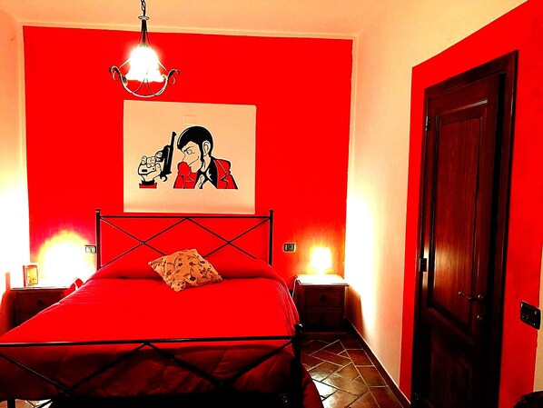 A room with a red wall, a bed with a black frame, a wooden door, and a painting of two people.