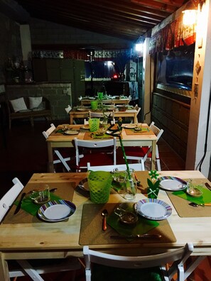 A dining area with tables set for a meal, chairs, and a television screen in the background.