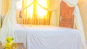 A room with a bed covered in a white sheet, a wooden door, and curtains. - Lolo Beach Inn (Legian)