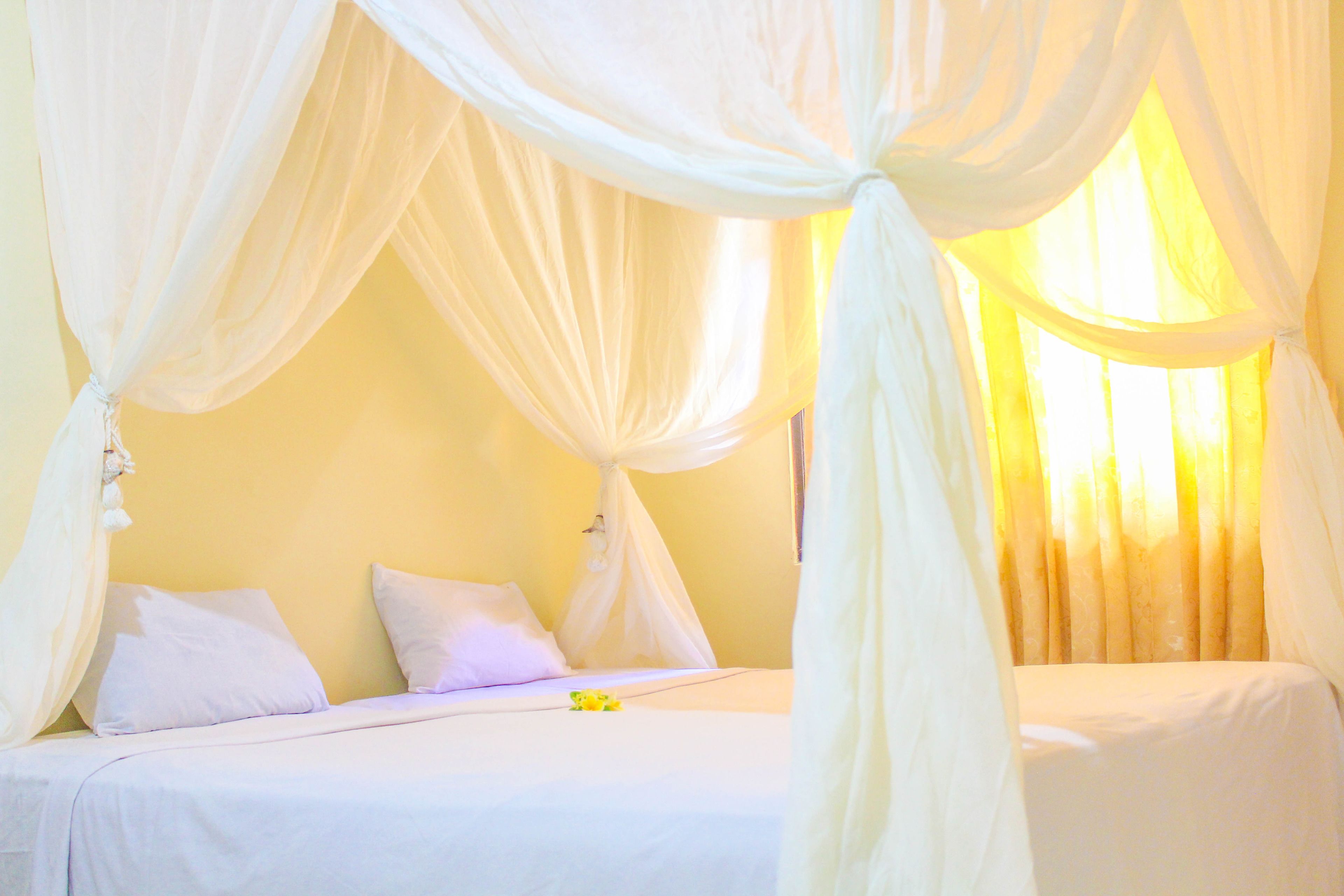 A room with a bed, white curtains, and a window with curtains.