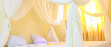 A room with a bed, white curtains, and a window with curtains.