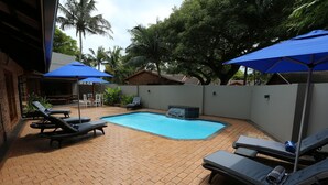 A backyard with a swimming pool, lounge chairs, and umbrellas.