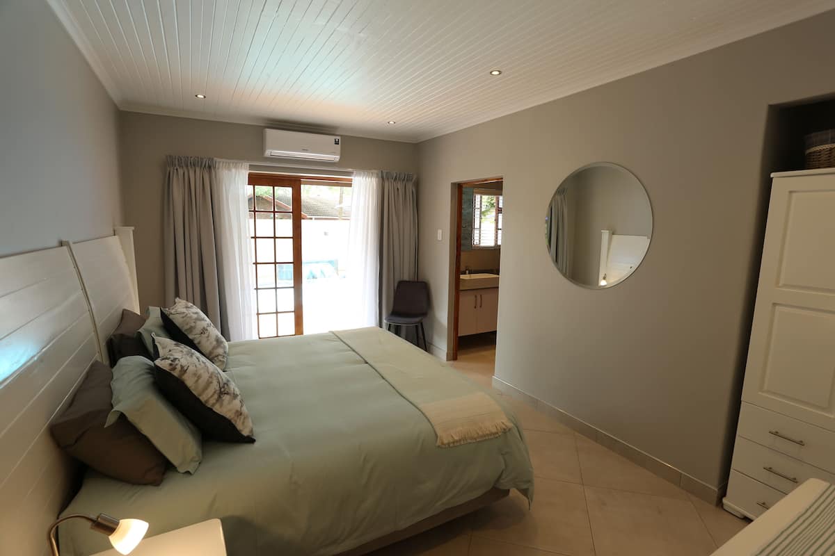 Um quarto com uma cama, abajur, espelho redondo e guarda-roupa.