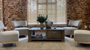 A cozy room with a brick wall, a wooden coffee table with a vase and books, and two patterned armchairs.