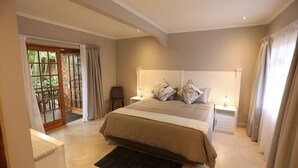 A bedroom with a large bed, a nightstand, a chair, and a view of the outdoors through a glass door.