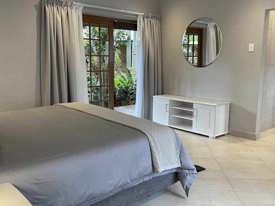 A bedroom with a large bed, a white console table, a mirror, and a view of greenery outside.
