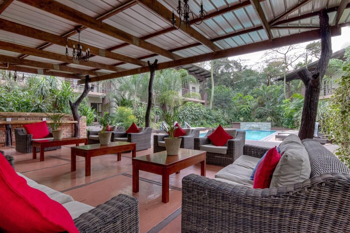 An outdoor lounge area with wicker furniture, red cushions, and a pool in the background.