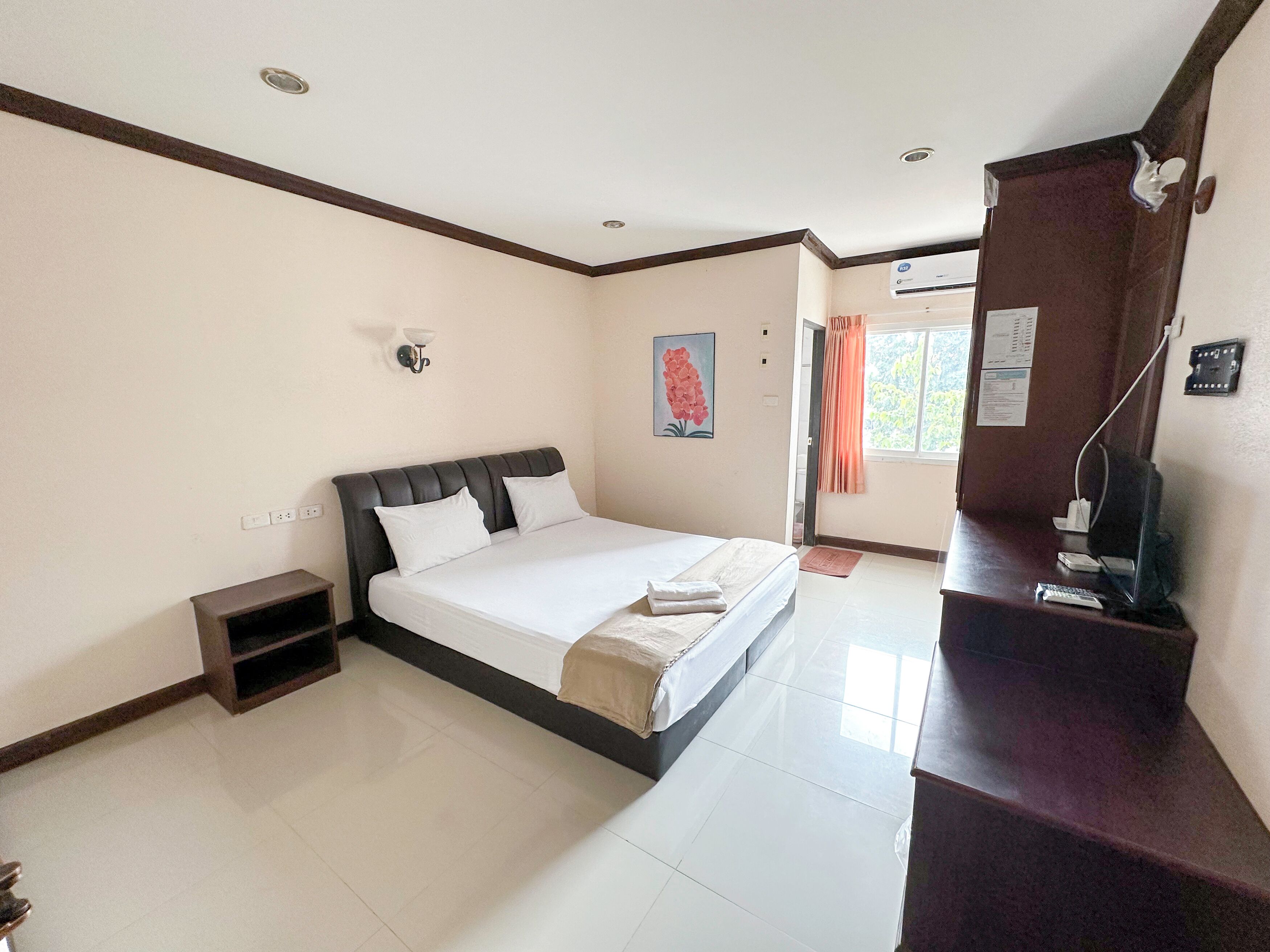 Une chambre d’hôtel équipée d’un lit, d’un bureau avec un ordinateur, d’une fenêtre avec des rideaux et d’un climatiseur fixé au mur.