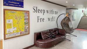 Un hall con un sofá de cuero marrón, una silla, un mapa en la pared y un letrero que dice “Duerme conmigo. ¡Wifi gratis!”