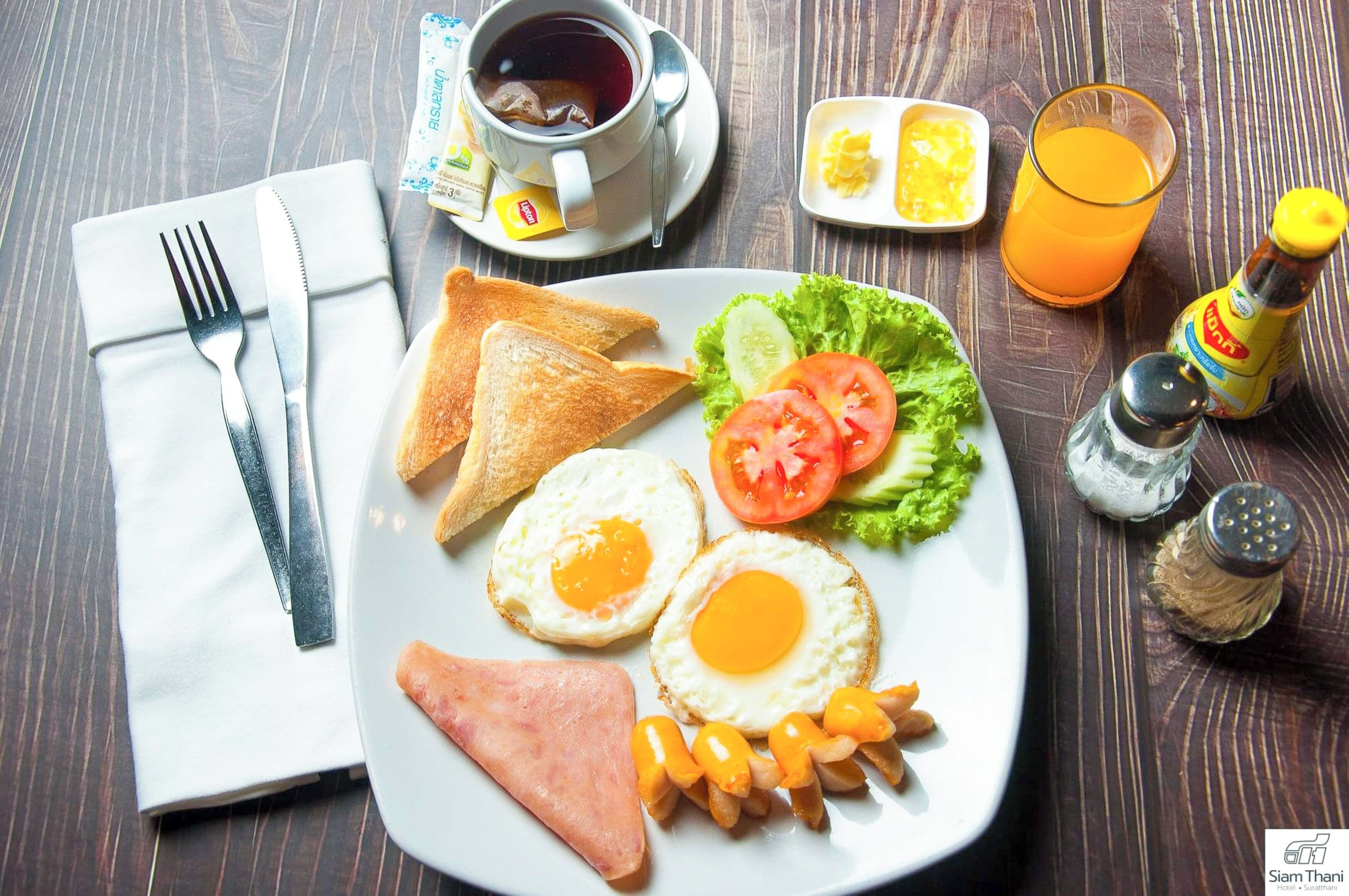 A breakfast plate with eggs, toast, ham, and fries, accompanied by a cup of tea, a glass of orange juice, and condiments.