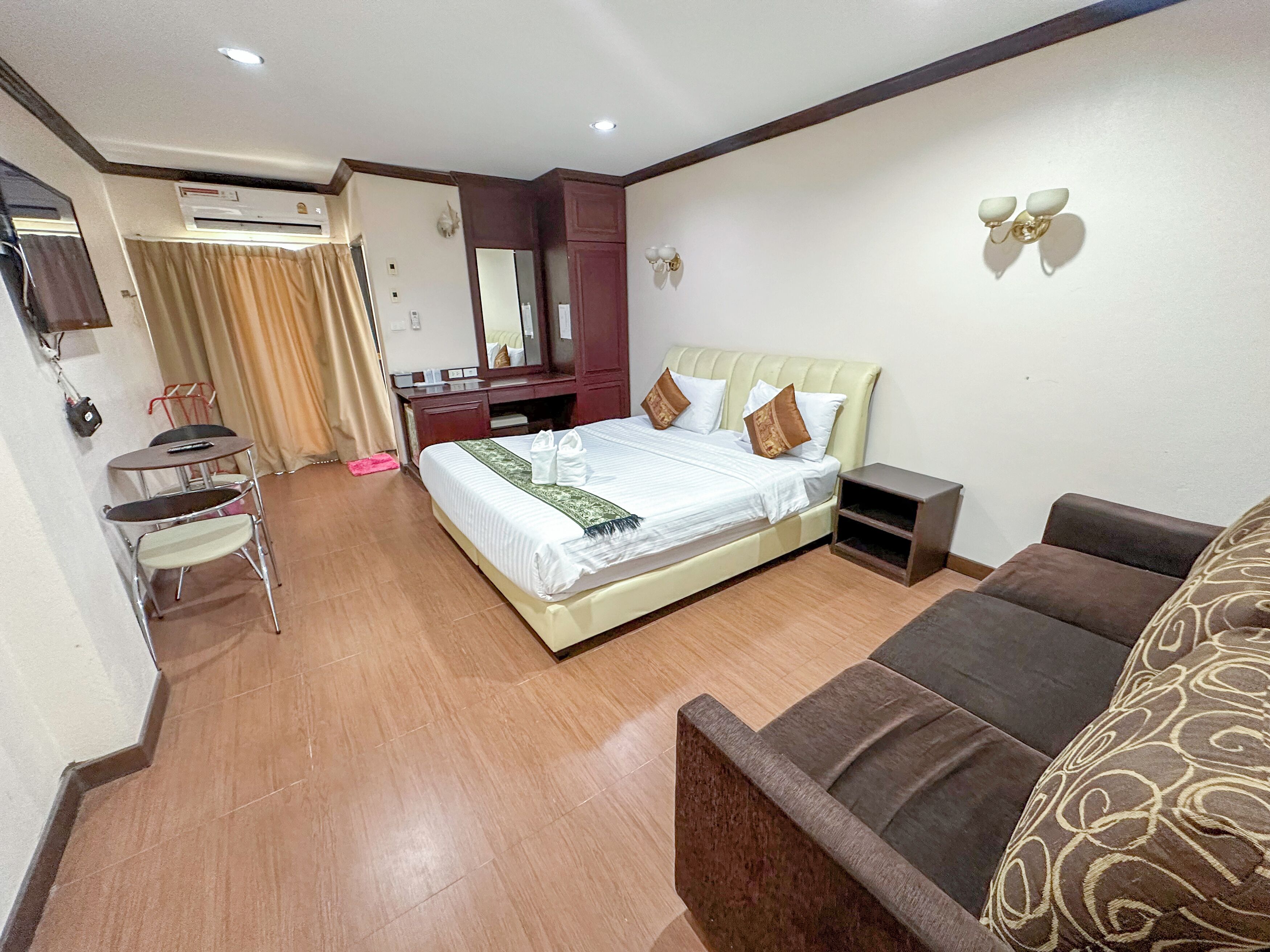 A hotel room with a bed, a desk, a chair, a sofa, an air conditioning unit, and a mirror.