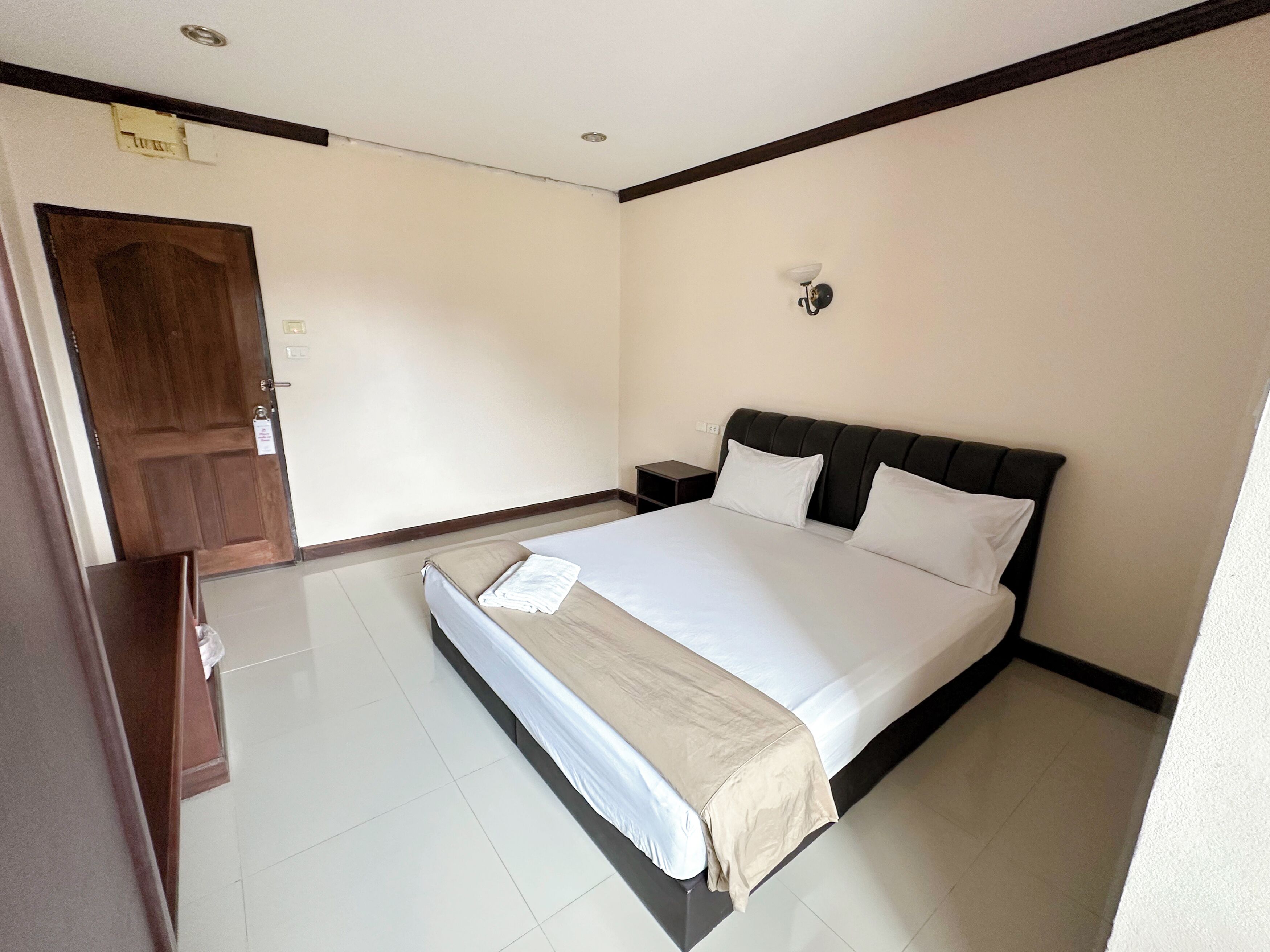 Una habitación de hotel con una cama, una mesita de noche, una lámpara de pared y una puerta.