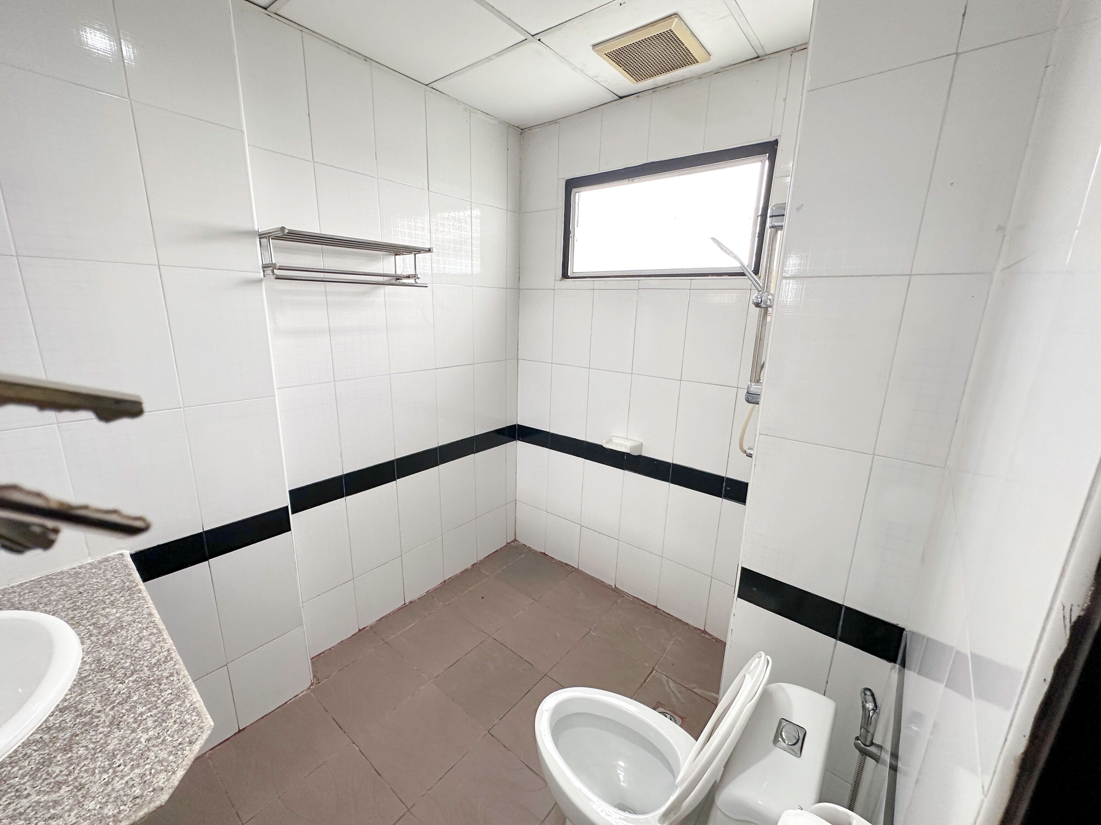 A small, clean bathroom with white tiles, a black stripe, a window, a toilet, and a sink.