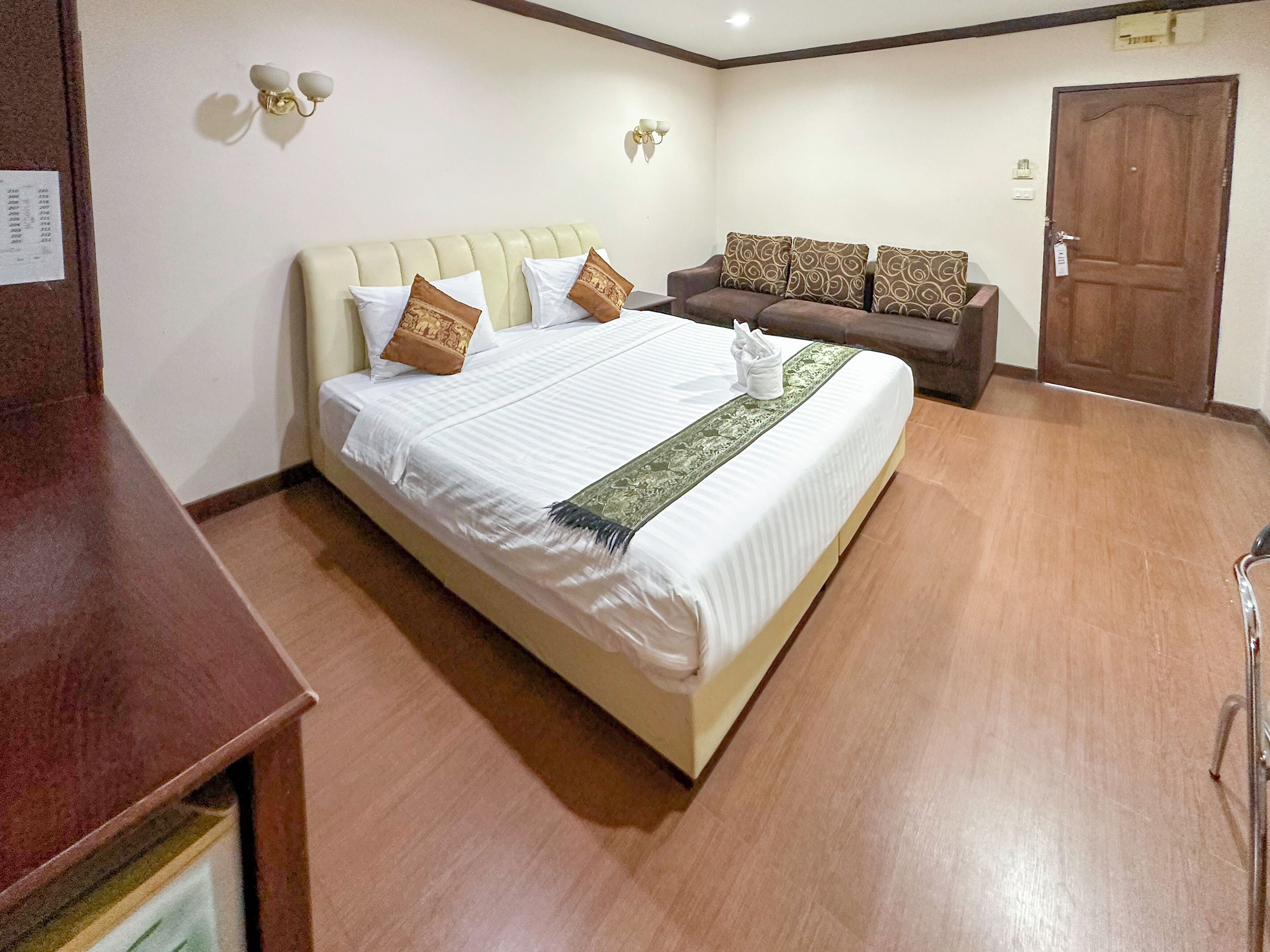A hotel room with a large bed, a sofa, a wooden floor, and a door.