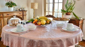 Una mesa de comedor con mantel rosa, fruta, pasteles y una preparación para café.