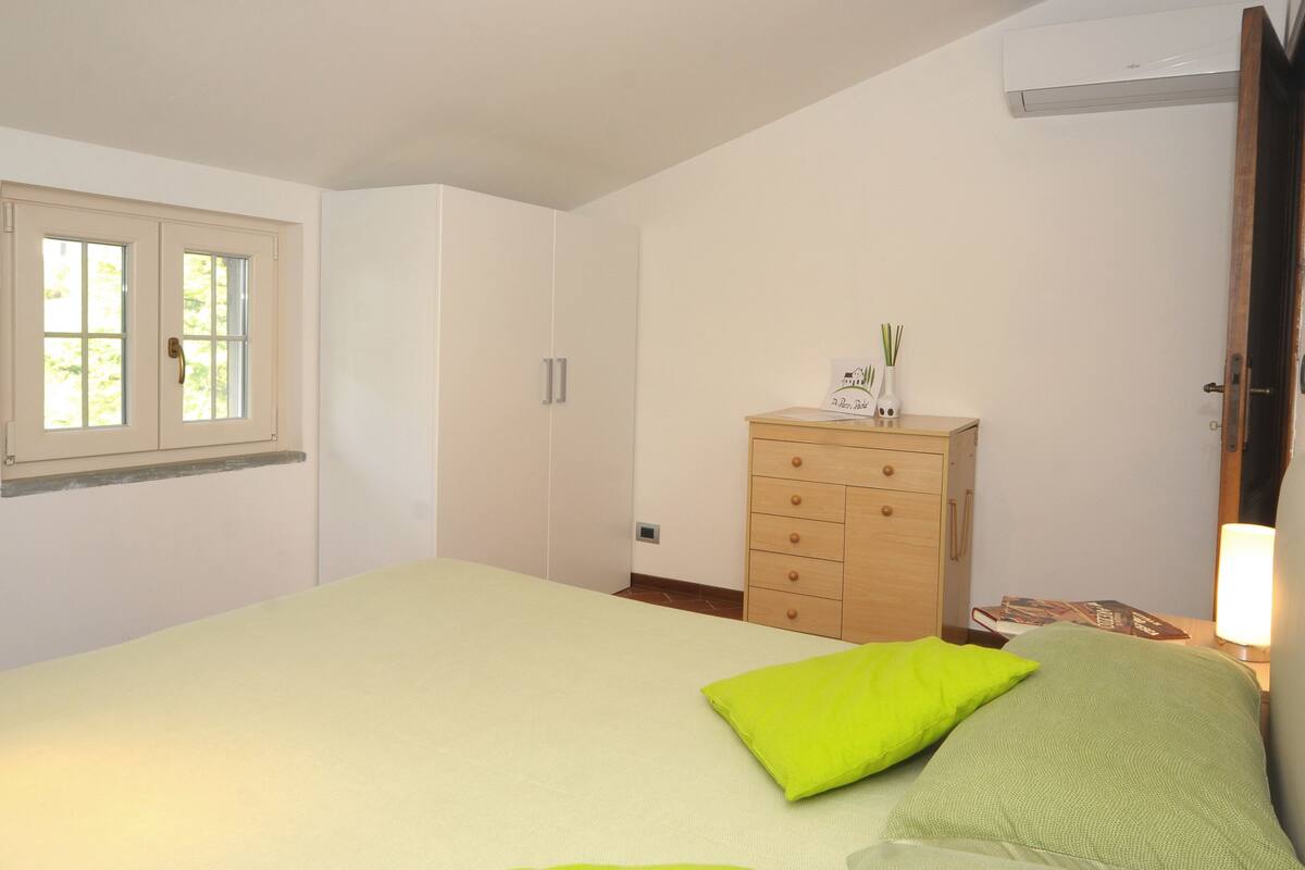 A bedroom with a bed, a dresser, a window, and an air conditioning unit.