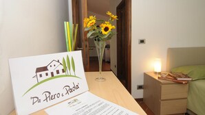 Una habitación de hotel con una mesita de noche de madera, una mesilla con lámpara, una cama con ropa de cama verde, un jarrón con girasoles y una tarjeta de bienvenida.