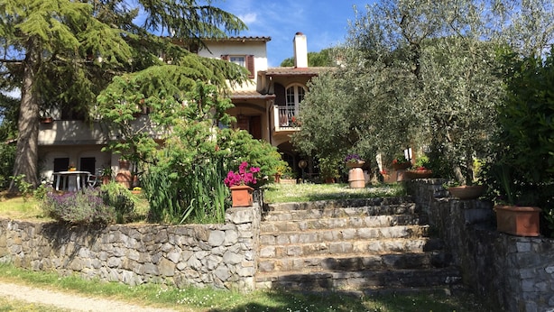 Una escalera de piedra lleva a una casa con techo de tejas, rodeada de exuberante vegetación y plantas en macetas.