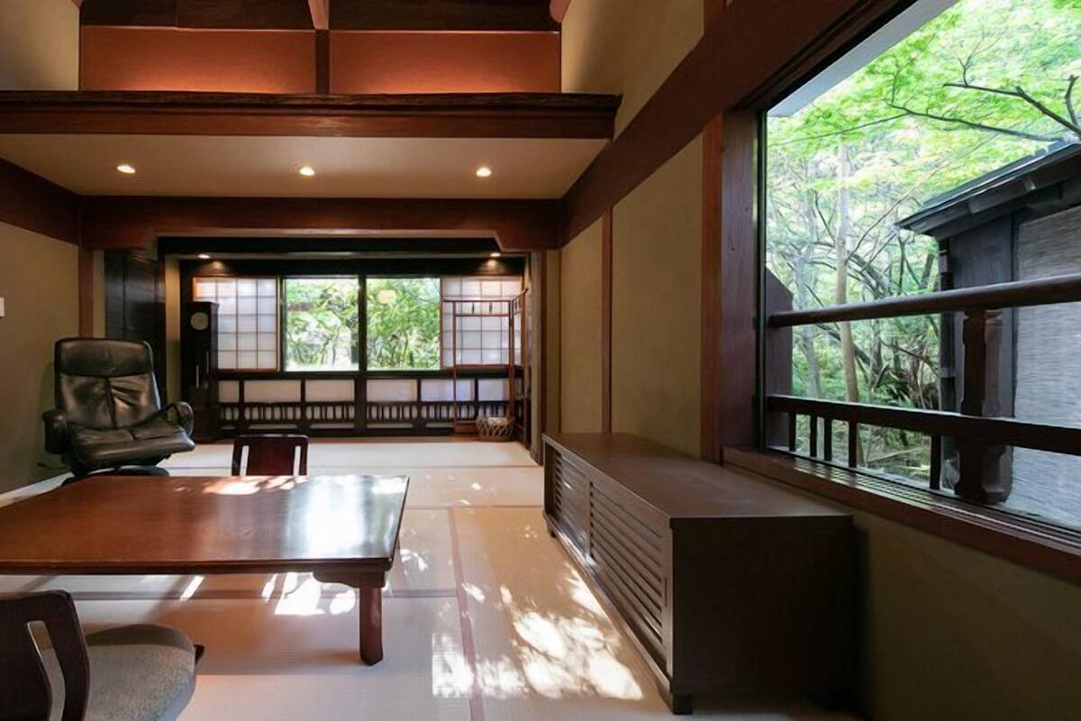 Una habitación tradicional japonesa con suelo de tatami, una mesa baja y vistas a la vegetación.