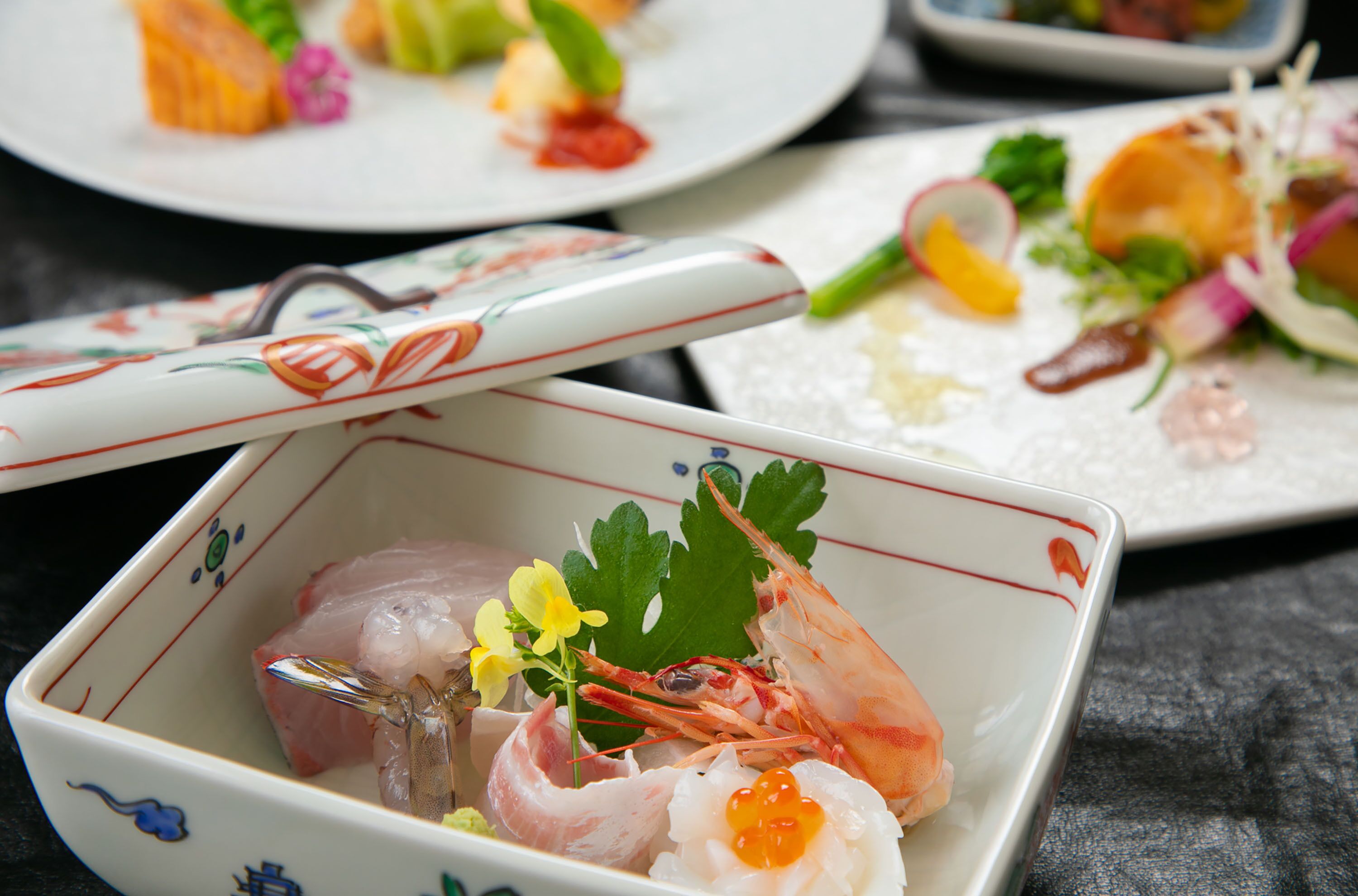 A square ceramic dish with a decorative pattern, containing a variety of seafood and garnishes.