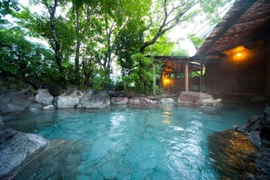 Una piscina cristalina rodeada de rocas y árboles, con una estructura de madera y un techo de paja al fondo.