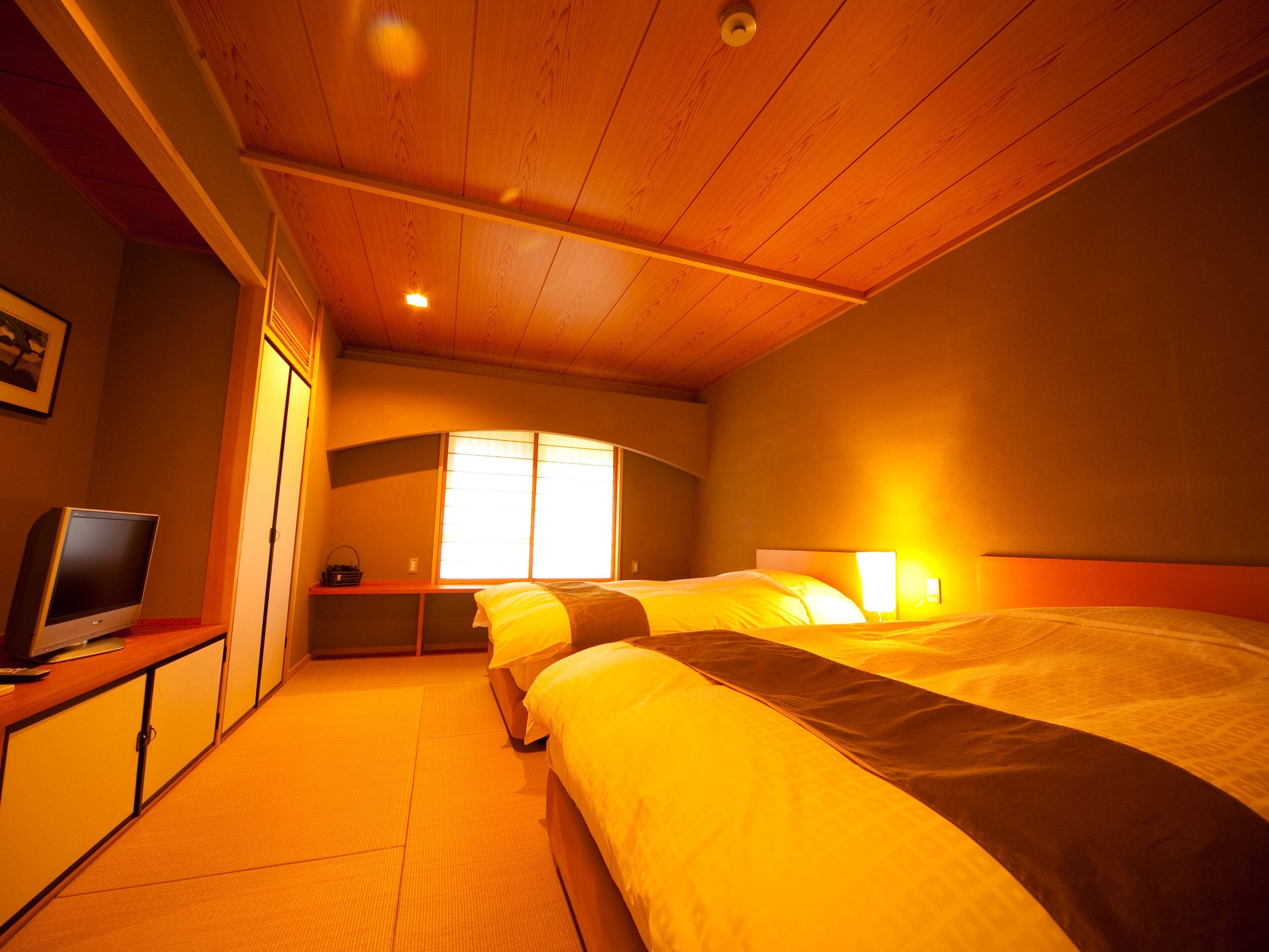 A hotel room with a wooden ceiling, a bed with white and brown bedding, a television on a wooden cabinet, and a window with blinds.