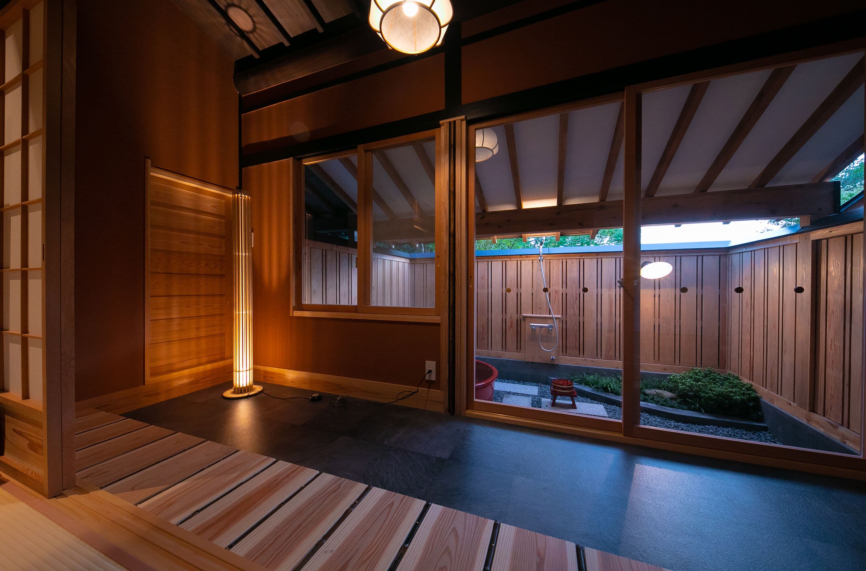 A traditional Japanese-style room with sliding doors, a wooden floor, and a small garden visible through the glass doors.