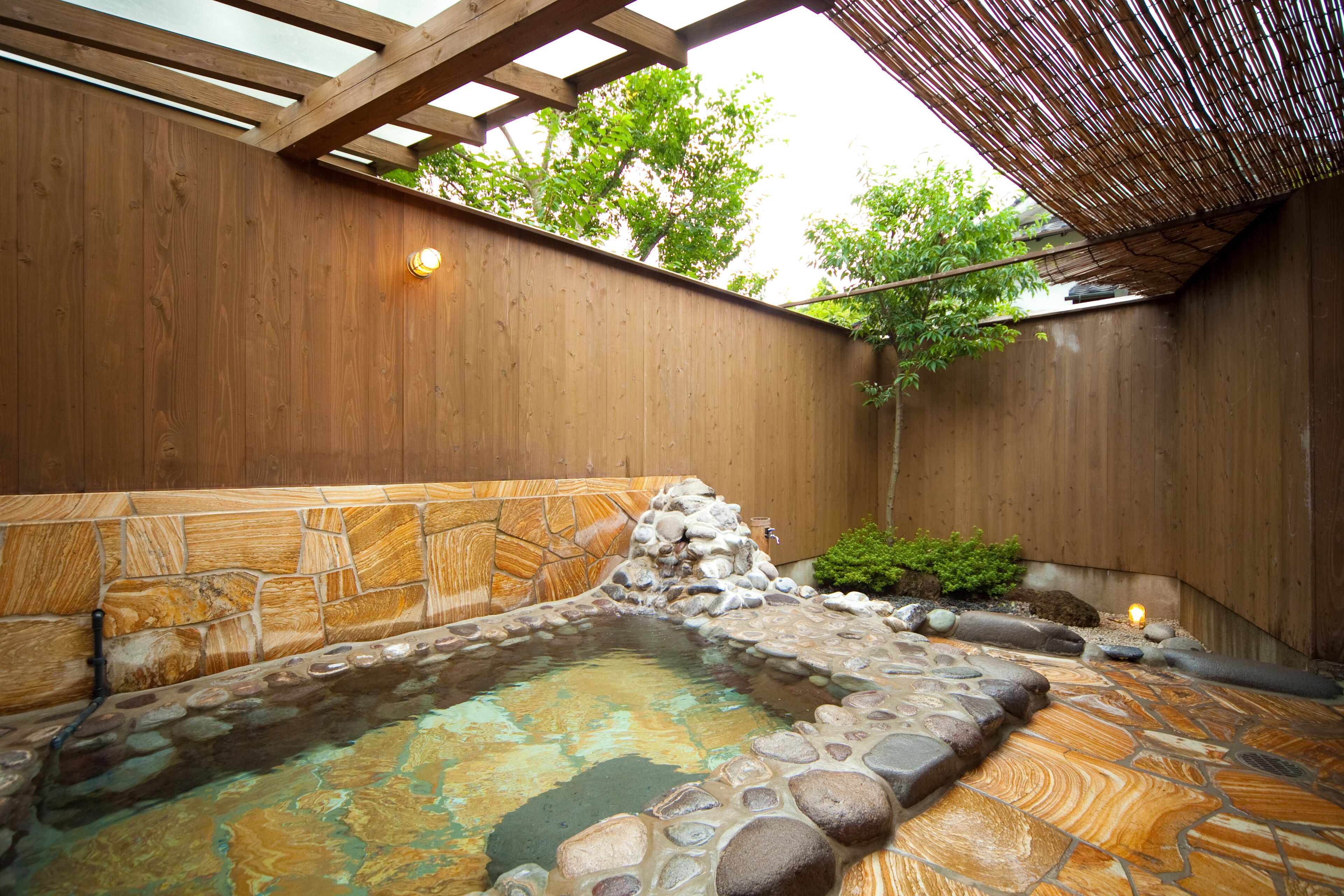 A hot spring area with a stone pool, wooden walls, and a bamboo roof structure.