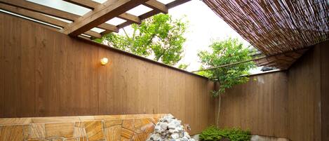 A hot spring area with a stone pool, wooden walls, and a bamboo roof structure.