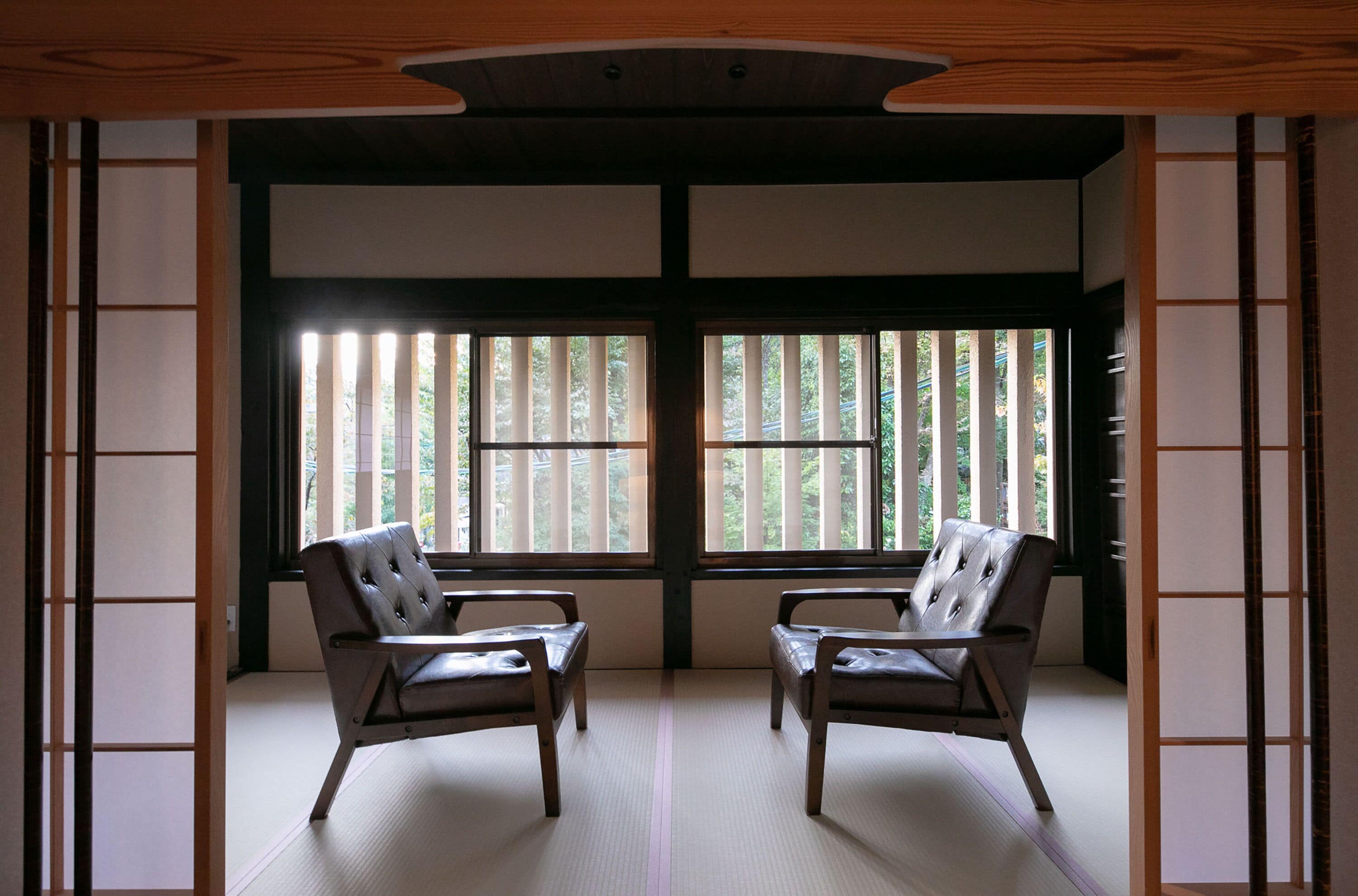 A traditional Japanese room with tatami flooring, two leather chairs, and sliding doors with a view of greenery outside.