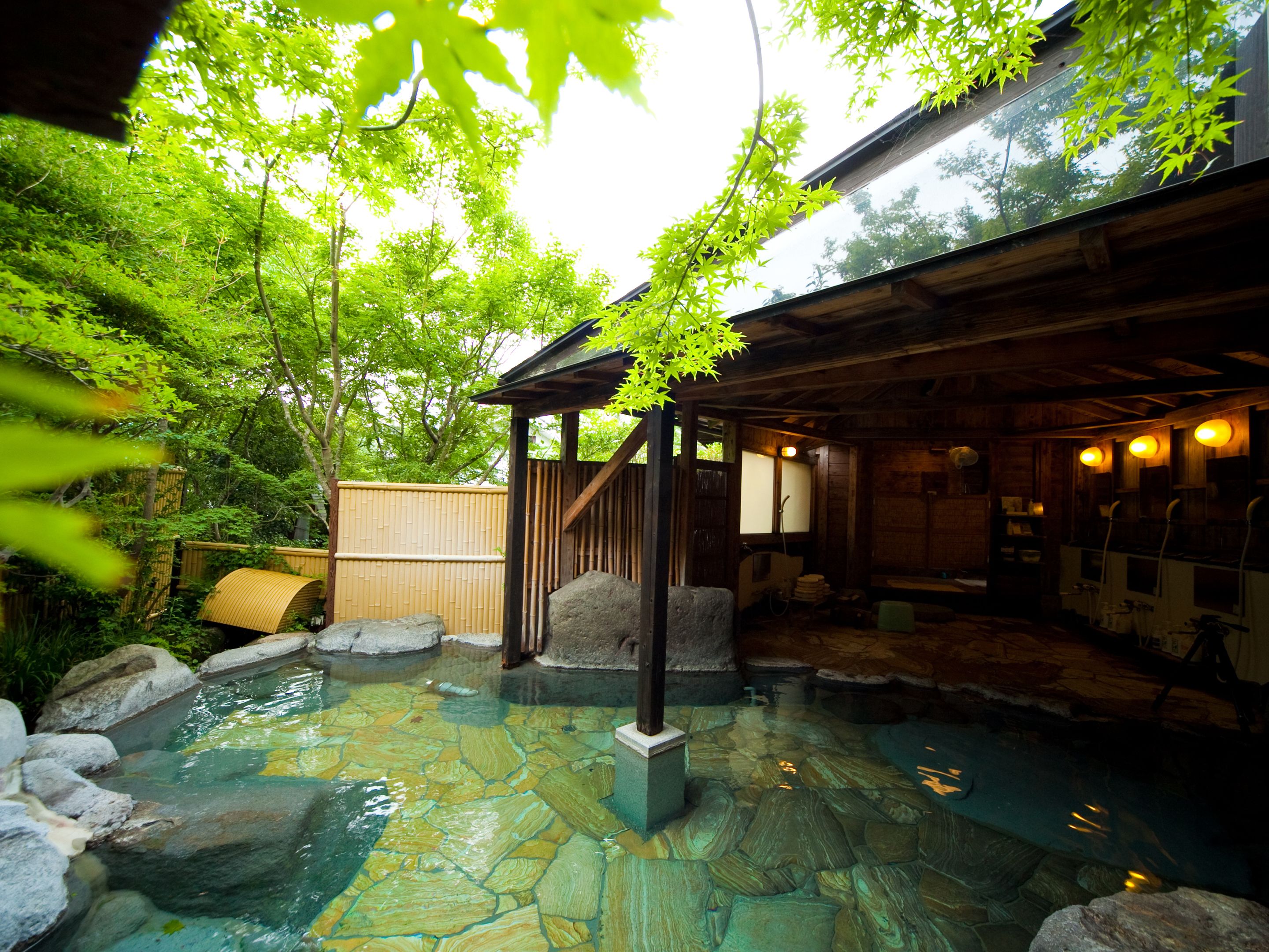 A traditional Japanese onsen with a stone bath surrounded by greenery and a wooden structure.