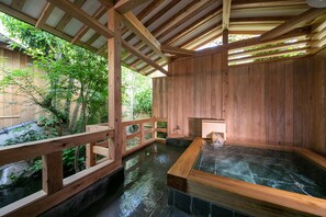 Un balneario de madera tradicional con aguas termales, vigas de madera y vistas a la vegetación.