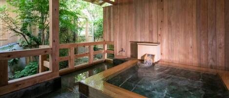 A wooden spa with a hot tub, wooden walls, and a view of greenery outside.