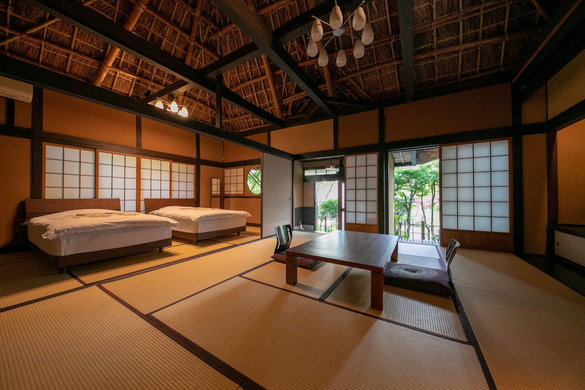 Una habitación tradicional japonesa con suelo de tatami, dos futones de tatami, una mesita baja y vistas a la vegetación.