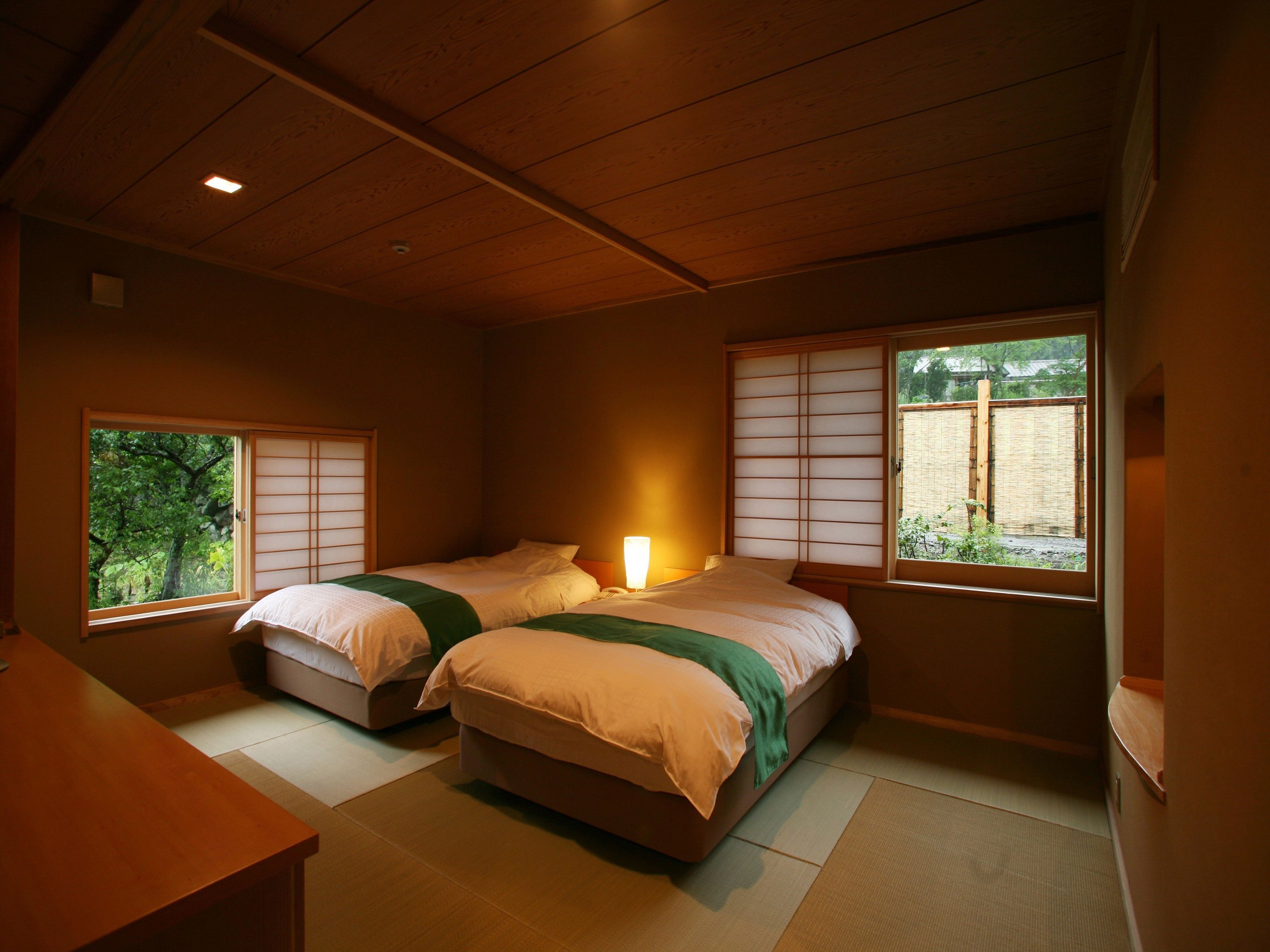 A traditional Japanese-style bedroom with tatami flooring, two beds with shoji screens, and a view of a garden.