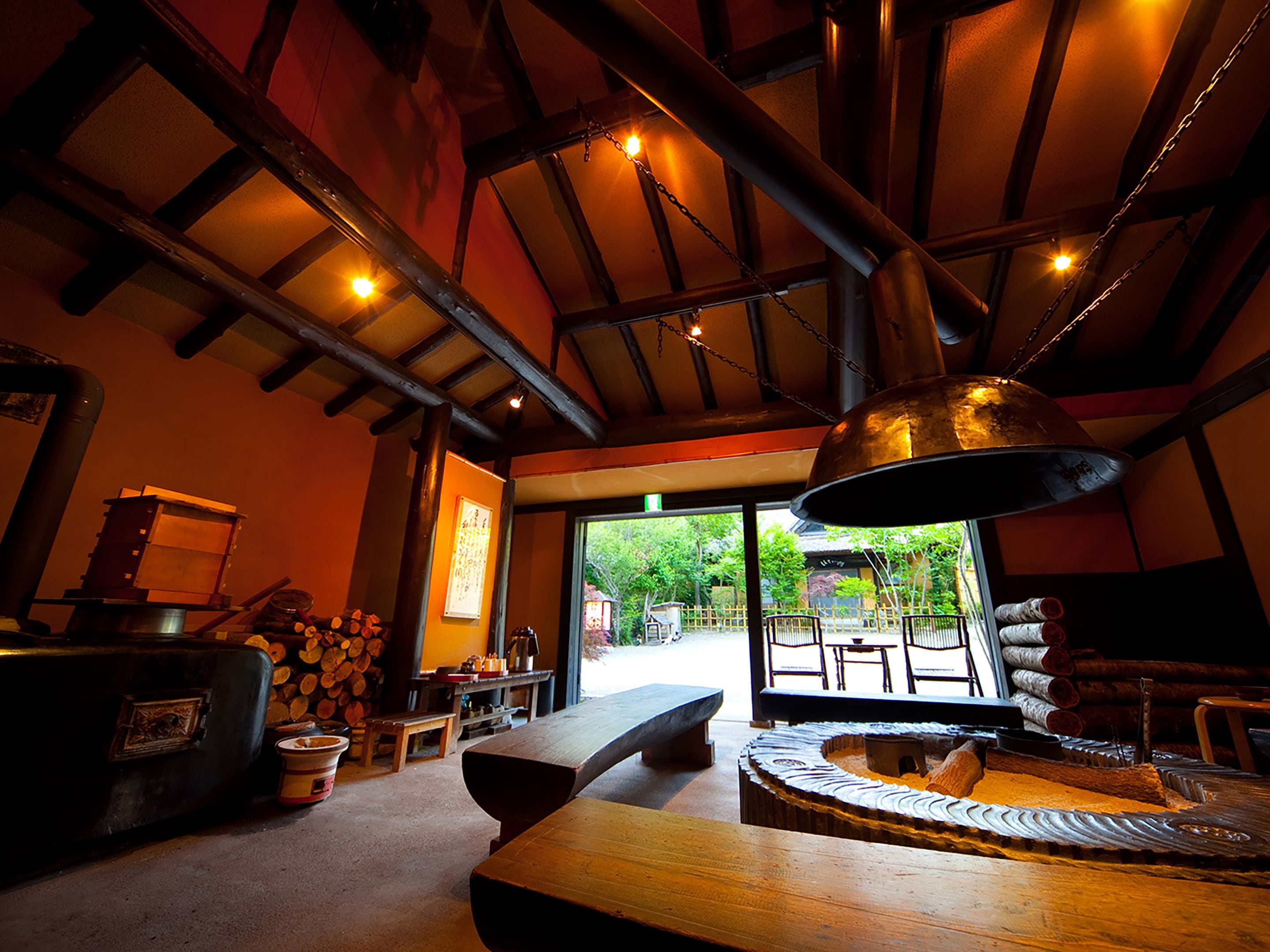 A rustic interior with a large wooden table, benches, and a stone fireplace.