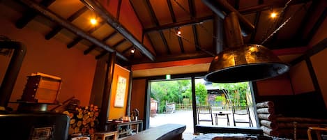 A rustic interior with a large wooden table, benches, and a stone fireplace.