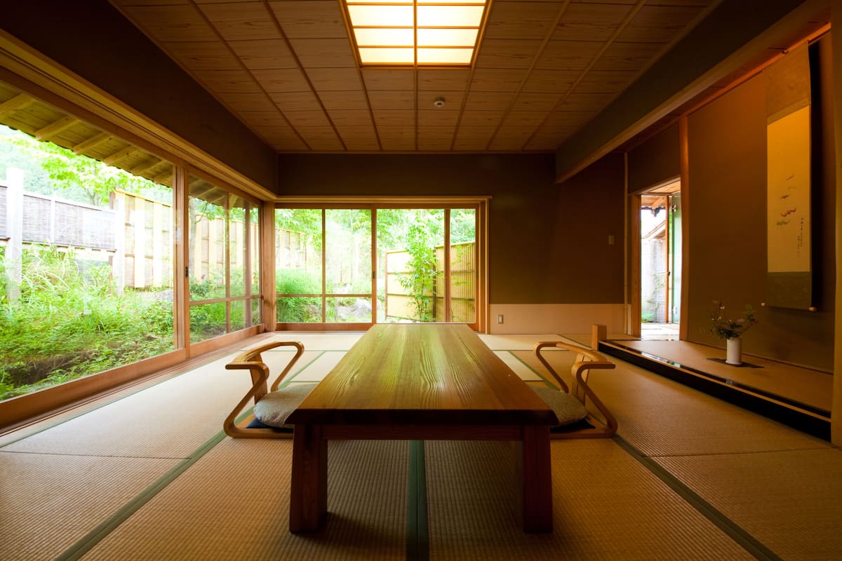 Una habitación japonesa tradicional con suelo de tatami, una mesa baja de madera y puertas correderas que dan a un jardín.