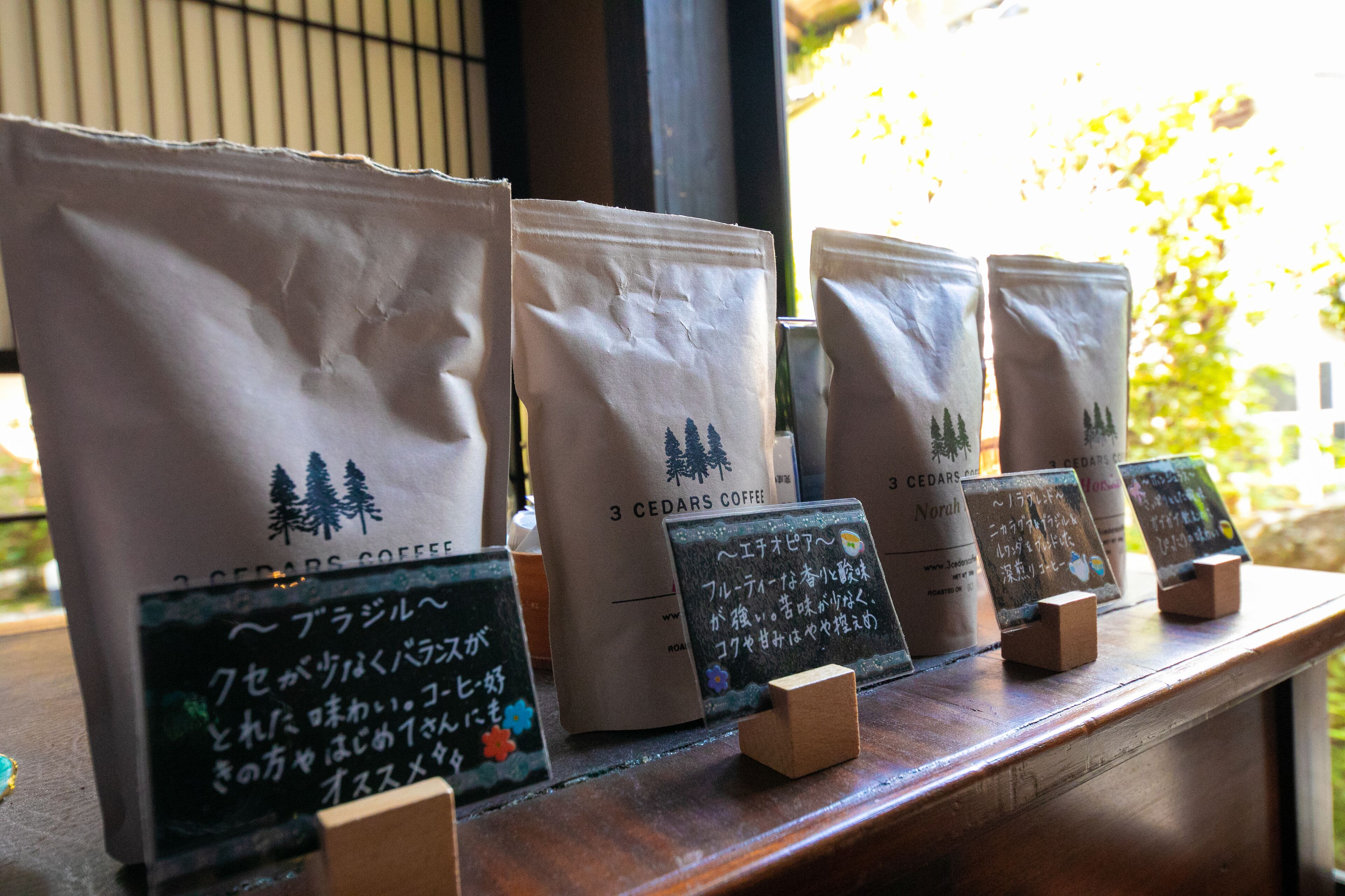Exposição de uma cafeteria com sacas rotuladas como "3 Cedars Coffee" e pequenas lousas com texto em japonês.
