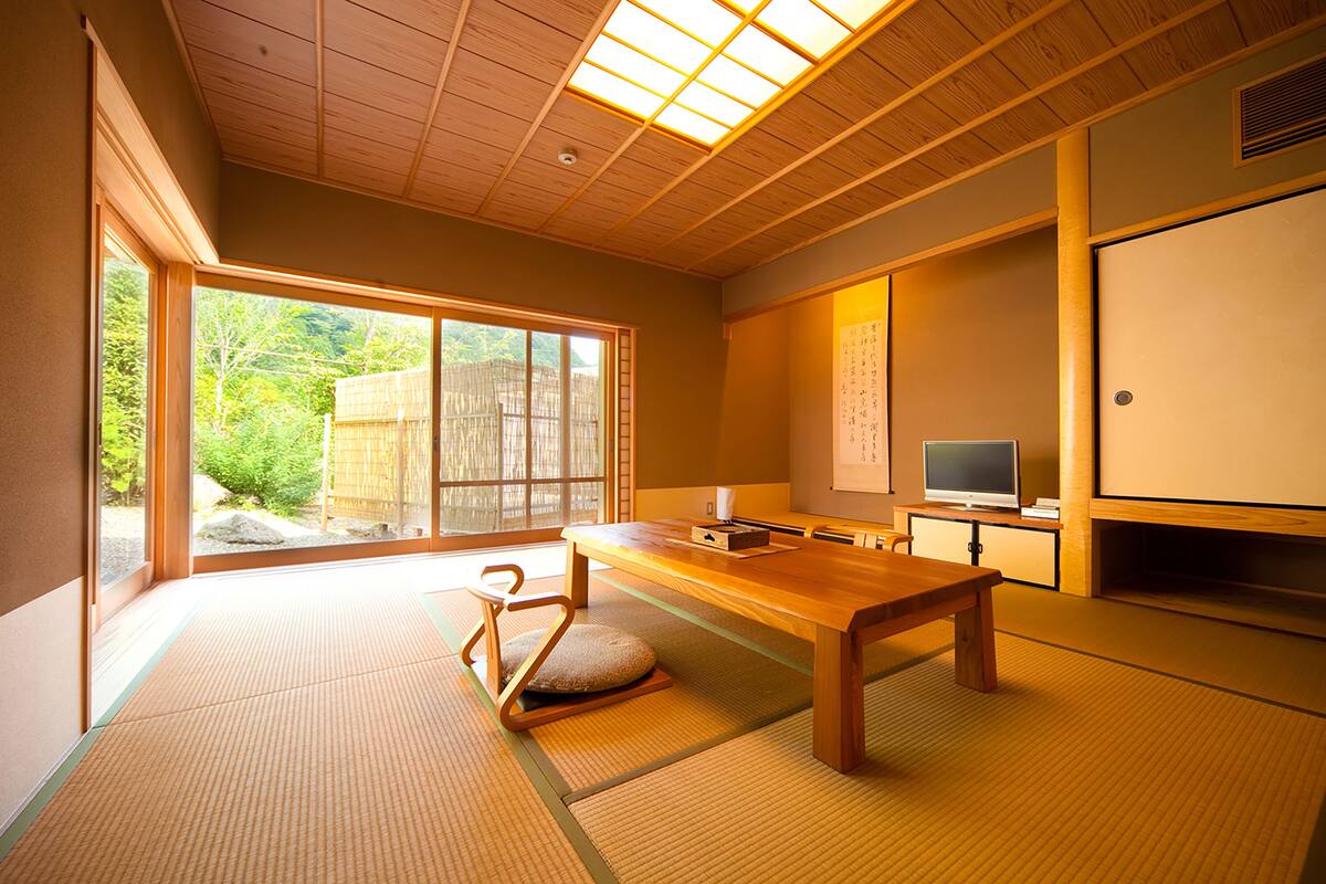 Una habitación japonesa tradicional con suelo de tatami, una mesa de madera baja, un televisor y una puerta corredera que da a un jardín.