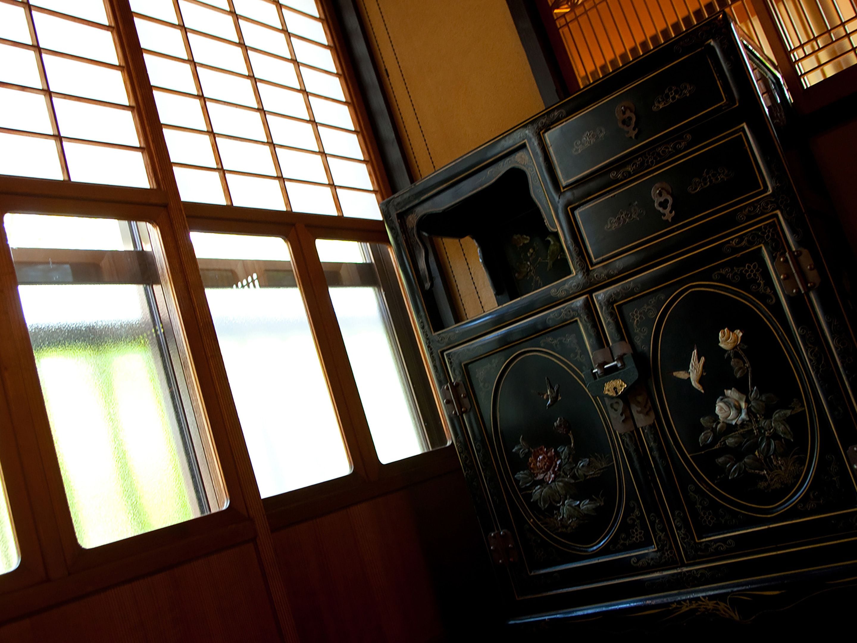 A room with a large window, a wooden cabinet with ornate designs, and a view of greenery outside.