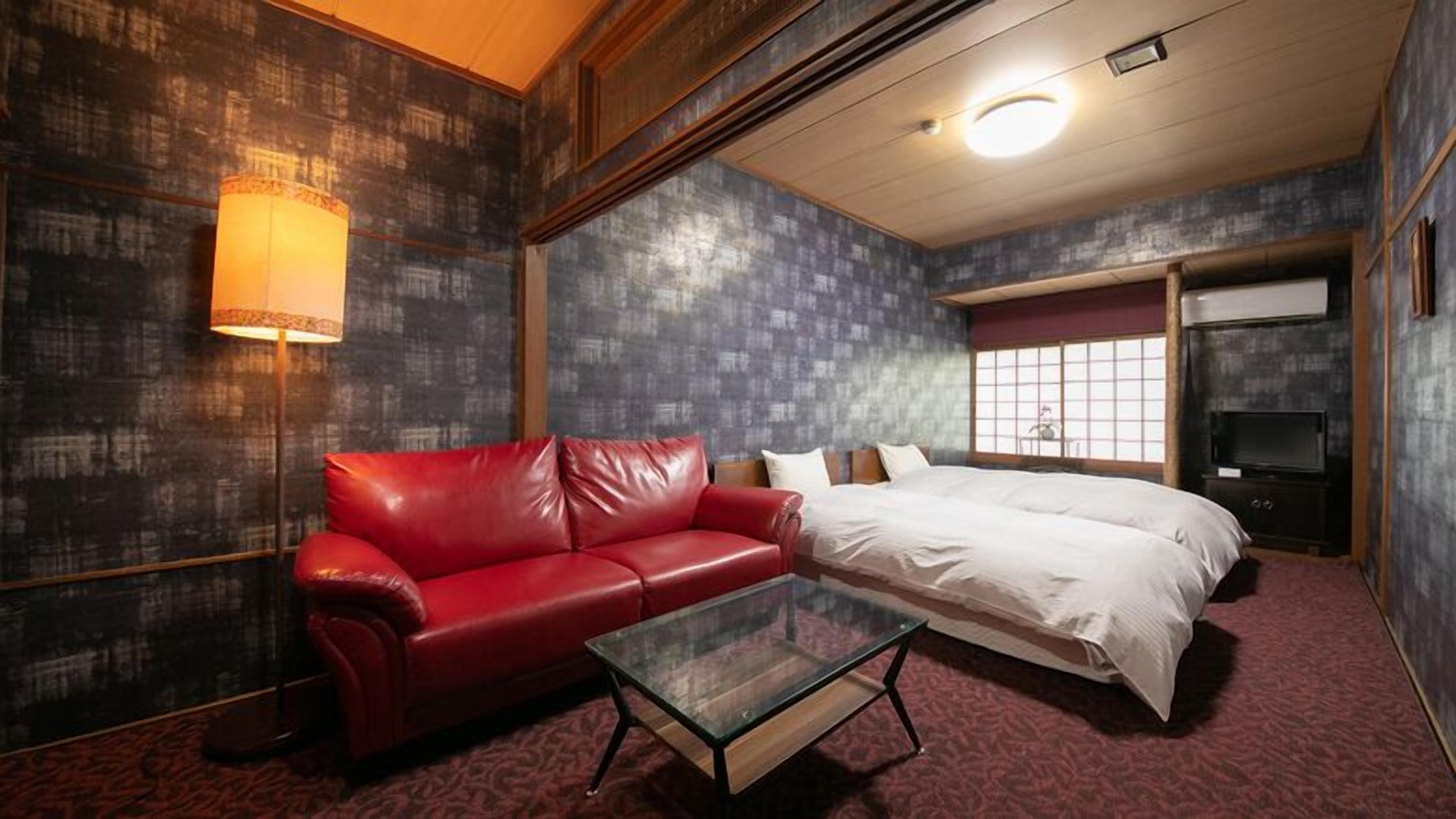 A hotel room with a red leather sofa, a glass coffee table, a bed with white linens, a television, and a large window with a view.