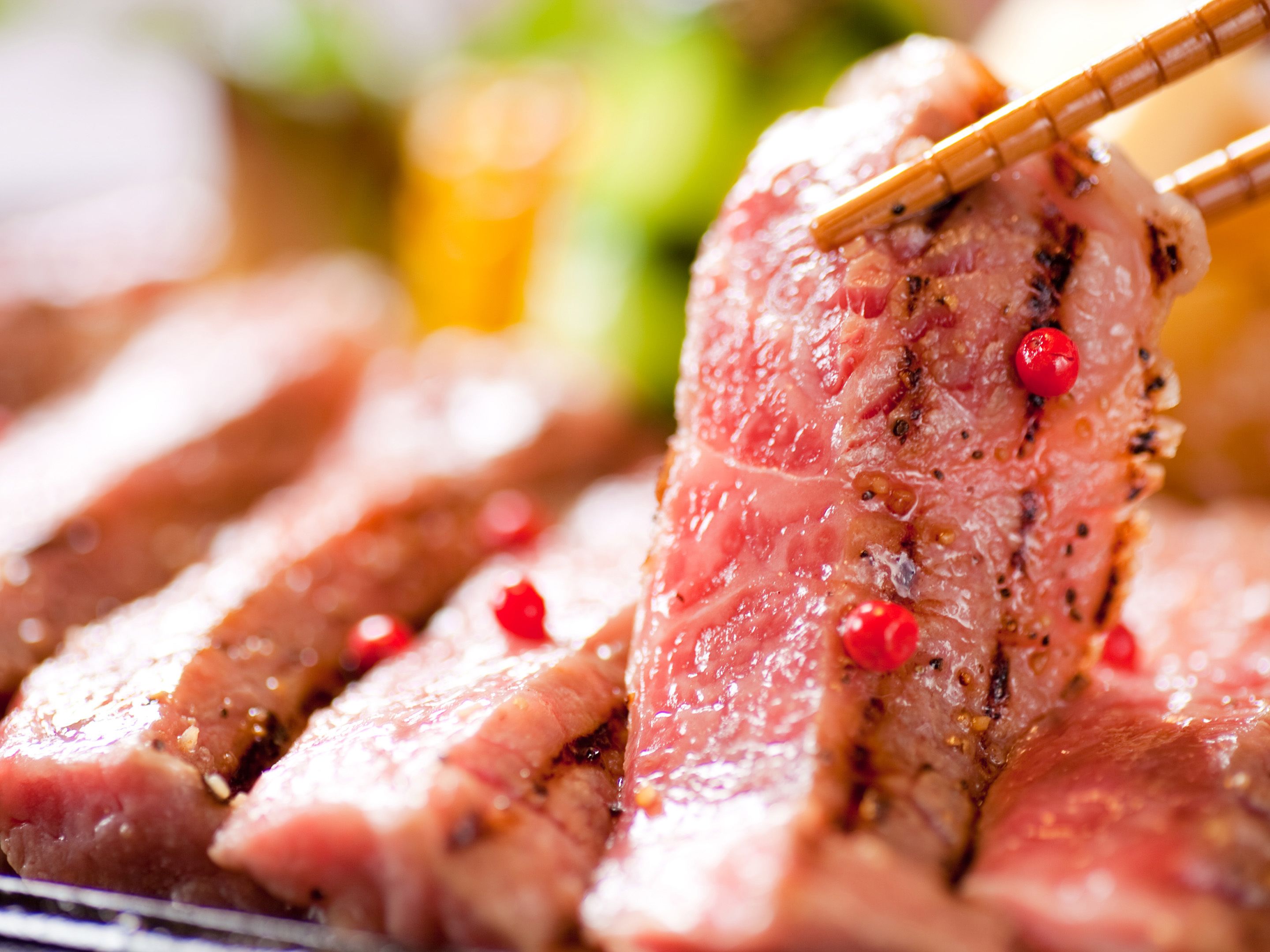 A close-up of sliced meat with chopsticks, garnished with red berries.