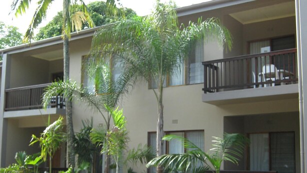 Un hotel de varios pisos con balcones, rodeado de plantas y flores tropicales.