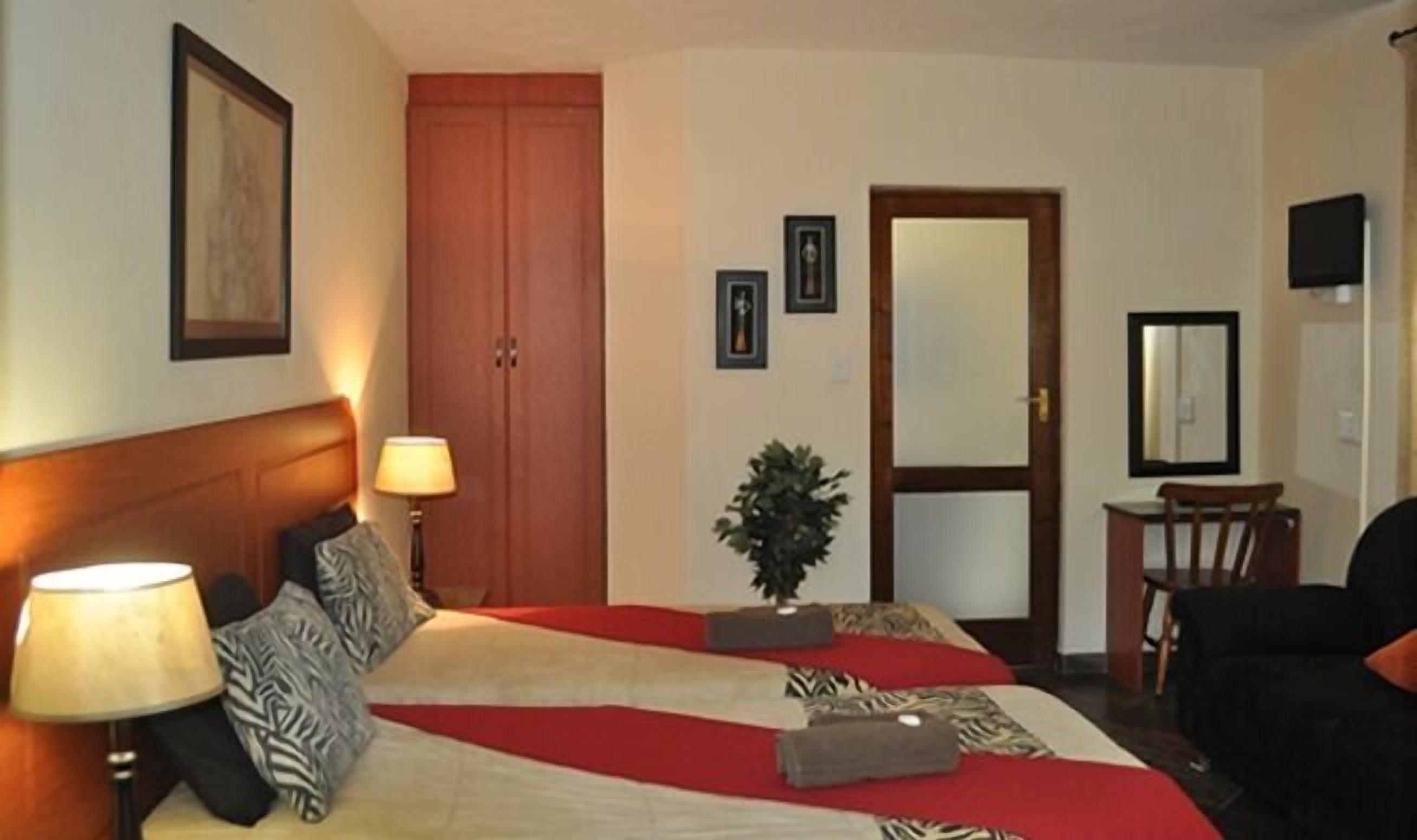 A hotel room with a bed, bedside lamps, a desk with a chair, a mirror, and a door.