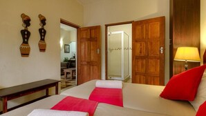 Habitación de hotel con dos camas, una puerta de madera, ducha y una mesita.