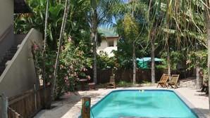 Una piscina rodeada de plantas tropicales y sillas de madera.