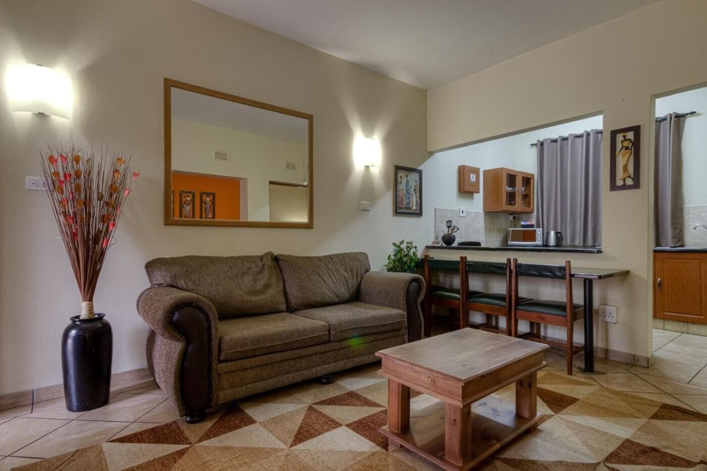 Ein Wohnzimmer mit einer Couch, einem Couchtisch, einem Esstisch mit Stühlen, einer Küchenzeile mit Schränken und einer Mikrowelle sowie einem großen Spiegel an der Wand.