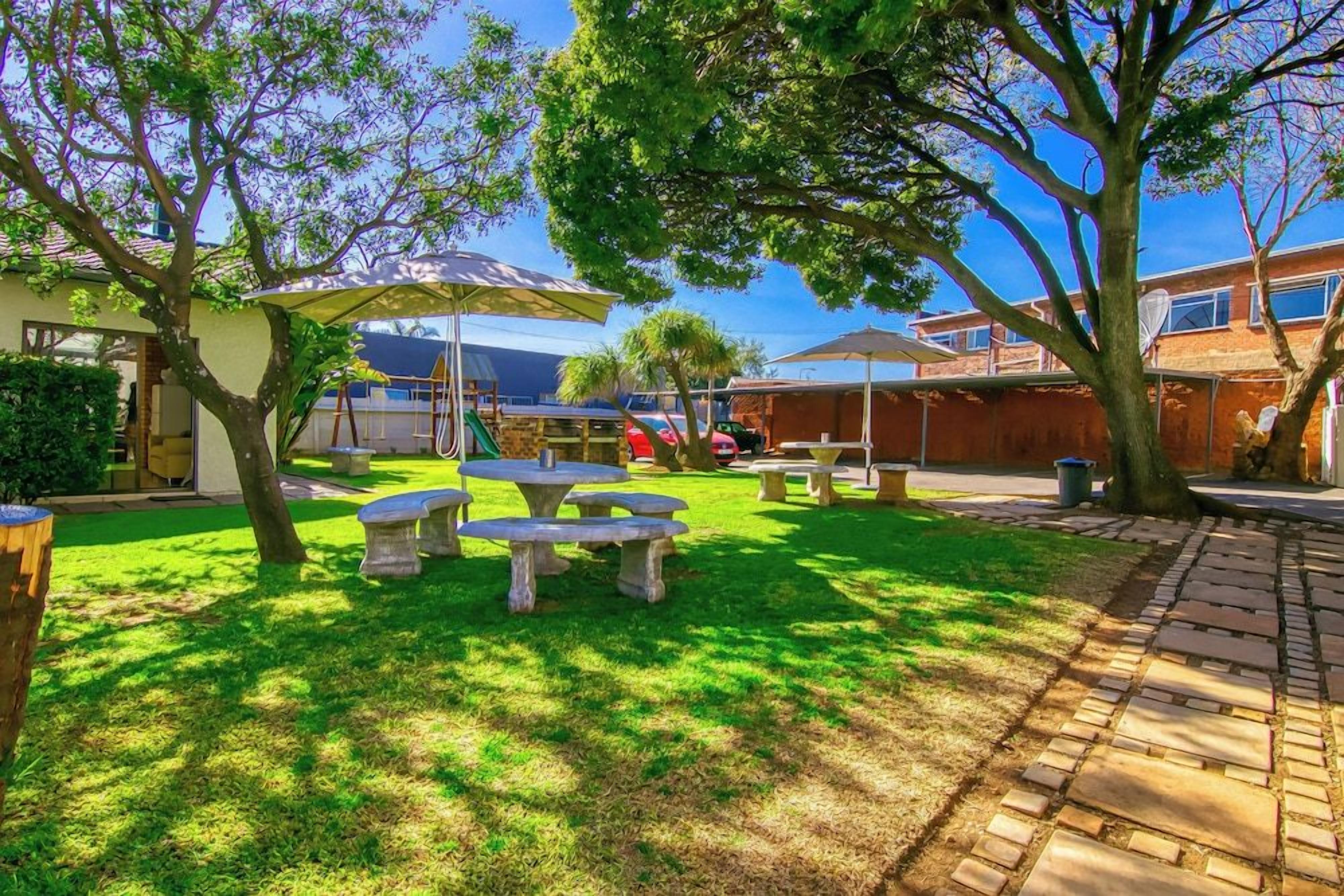 A backyard with a picnic table, a covered seating area, and a brick pathway.