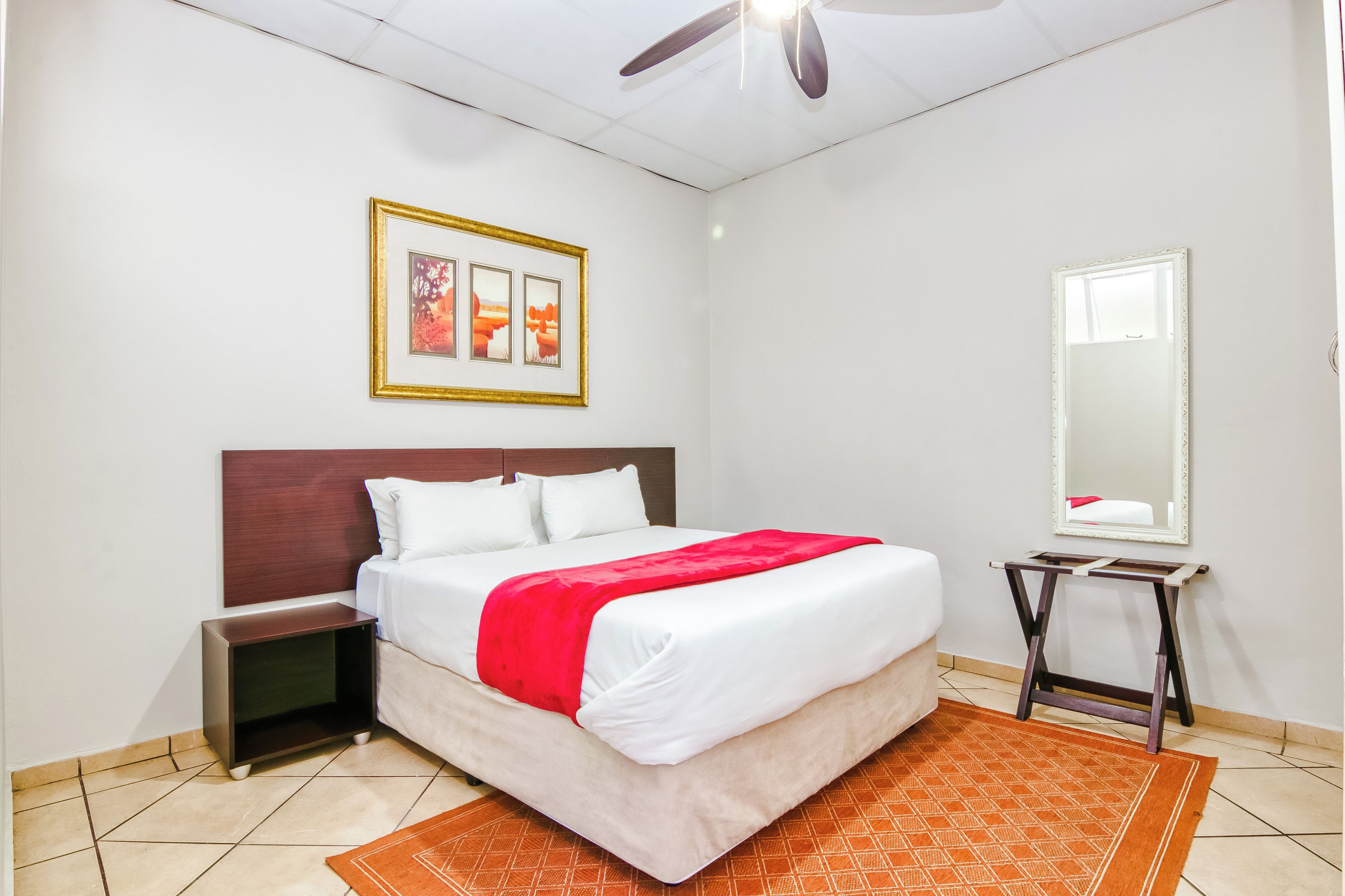 Quarto de hotel bem arrumado com cama, mesa de cabeceira, espelho e um quadro na parede.
